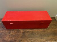 Closed rectangular red wooden toolbox with visible age wear on surface, placed on dark wood table.