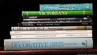 Stack of nine hardcover and paperback books about antiques, decorative arts, silver, Fabergé, and boxes on a dark wooden surface.