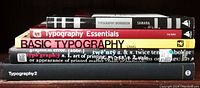 Books stacked showing spines with titles 'Typography Essentials', 'Basic Typography', 'Typography Workbook', and others