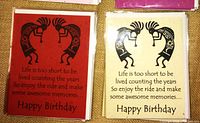 Close-up of two Happy Birthday cards with identical design of stylized Kokopelli figures forming a heart, one on red paper and one on off-white paper.