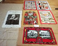 Five tea towels displayed on a wooden surface. Designs show Shakespeare portrait, London A-Z, Royal London, Silver Jubilee, and South Devon themes.