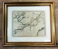 Front view of framed antique map inside a gold-colored frame on a textured surface showing the map area of Upper and Lower Canada and an inset.
