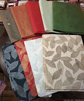 Sheets of assorted Saa (mulberry bark) paper and decorative papers including solid colors and leaf motif prints in multiple colors laid out on a surface.