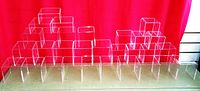Front view of multiple clear acrylic risers arranged in three rows against a red background showcasing various sizes and shapes.