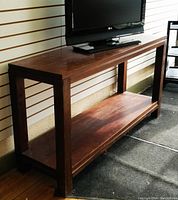 Full side view of the solid wood console table showing structure, surface finish, and lower shelf. A television is placed on top for scale.