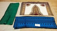 Three fabric pieces displayed flat on wooden floor: green fabric with stripes, beige fabric with maroon ornate pattern, black and blue fabric with linear motifs. Includes lot number card 160.