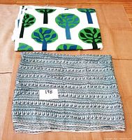 Two folded fabric remnants on a tan surface. One fabric has a print of stylized trees in blue and green on white, the other is turquoise with peacock motifs in white and black.