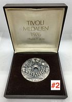 Opened presentation box showing the front side of the sterling silver medallion with intricate relief artwork featuring Tivoli Gardens elements, crowds, and flags. The box interior lid displays 'TIVOLI MEDALJEN 1976 HELMUT ZOBL' in gold script.