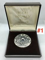 Medallion inside original box showing front with Tivoli entrance and crowd relief design. Box lid satin interior reads 'TIVOLI MEDALJEN 1976 HELMUT ZOBL'.
