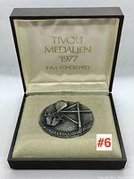 Two open medallion boxes showing the medallions and their presentation boxes with inscriptions of year and designer.