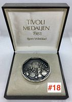 Closed view of the first octagonal sterling silver Tivoli medallion in a black presentation box with satin interior and gold lettering of 'TIVOLI MEDALJEN 1981 Bjorn Wiinblad'.