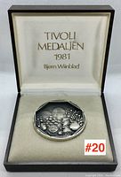 Medallion inside original box shown from above, showing interior text imprinted on silk lining with the medallion centered on a cushioned area.