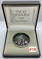 Two high detail images of one octagonal sterling silver medallion showing elaborate floral and face motifs with dark oxidation and polished edges, placed in velvet-lined presentation box with satin lid text.