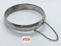 Front angle showing engraved floral pattern and chain attached to clasp.