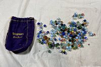 Marbles spread out next to a purple velvet Seagram's Crown Royal pouch embroidered in gold.
