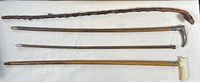 Four wooden canes/walking sticks laid side by side displaying variation in length and handle styles.