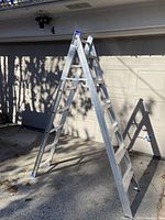 Angle view of aluminum step ladder opened in A-frame position on driveway in front of garage.