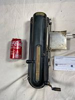 Top view of antique cheque printing machine in black metal with crank and feed slot, shown next to a Coca-Cola can for size reference.