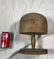 Photo of entire wooden hat stand next to a soda can for scale, showing the dome top, spindle, and circular base.