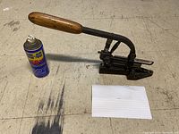Wide shot of the full antique stapler machine with wooden handle, alongside a WD40 can and an index card for scale.