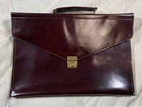 View of the front of the burgundy maroon leather portfolio case showing the envelope-style flap with brass lock and smooth leather surface.