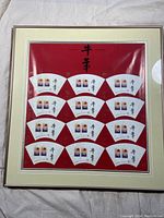 Full view of the framed stamp sheet showing 12 fan-shaped stamp card sections on a red background inside a cream and silver border frame.