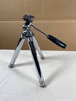 Front view of chrome camera tripod with handle for adjusting camera mount