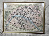 Full view of the framed stylized map of Paris monuments showing the layout and location of monuments in Paris. Frame is gold-colored and glass is cracked.