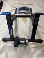 Indoor bicycle exercise stand frame lying flat on a fabric surface, showing Tacx logo and blue adjustment knobs.