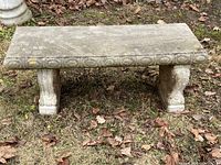 Full front view of one concrete garden bench on grass with oak leaves, showing simple top with oval edge detail and two scroll style legs