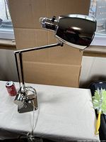 Full side view of the chrome swing arm desk lamp with geometric solid base and adjustable head.