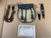 Photo showing the sporran, dagger with leather sheath, and certificate all together on a cardboard background.