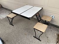Folding picnic table set up with four attached seats surrounding the table, shown outdoors on pavement.