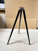 Black tripod extended standing with three legs, against cardboard background.