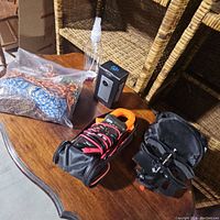 Table surface showing the braided cords in a plastic bag, clear spray bottle, Flip camera box, Fluke clamp meter in case