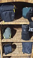 Shelf display showing six assorted carrying bags and pouches in black and green, varying in size and design.
