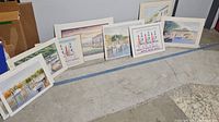 View of all nine framed beach prints arranged on the floor showing varied coastal scenes including piers, boats, and beach houses.