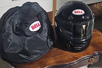 Full view of Bell black full face motorcycle helmet with clear visor and black Bell logo carrying bag on wooden surface.