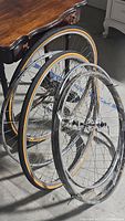 Six bicycle rims shown, four without tires, two with tan sidewall tires mounted. All rims with spokes and hubs visible.