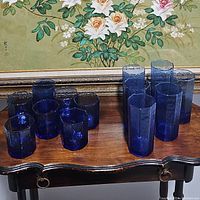 Front shot of seven small tumblers and six taller hexagonal drinking glasses made of deep blue glass with textured pattern.