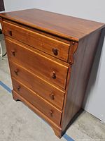 Front angled view of the four drawer wooden chest showing drawer knobs and surface wear.