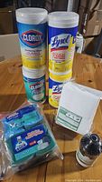 Photo showing two containers of Clorox disinfecting wipes, two containers of Lysol disinfecting wipes, a pack of white eraser sheets, a bottle of eucalyptus oil, and a pack of Mr. Siga sponges.