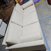 Full view of cream sofa showing clean lines and dark feet in a warehouse setting.