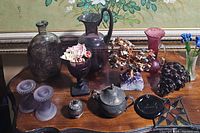 Full lot on wooden surface with various decorative items including pitchers, candle holders, metal teapot, crystal cluster, glass bottle, and floral arrangements.