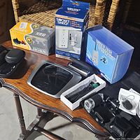 View of the entire lot on a wooden table showing various boxed items and electronic accessories including horn, camera kit, socket shelf and remote.