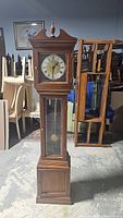Full view of tall grandfather clock with wooden case and pointed top finial.