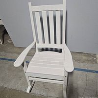Front view of white wooden rocking chair showing slatted seat and backrest, armrests, and rockers.