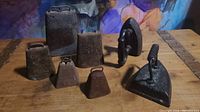 Photo showing all five metal bells and two cast irons on a wooden surface with artistic background, highlighting the rustic and aged characteristics of the items.