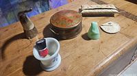 Six assorted vintage items displayed on wooden surface: shaving mug with brush, horn-shaped pipe, leather pouch, green vase, round tin box, white pouch.