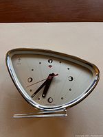 Front view of the 1950s Polaris alarm clock showing triangular chrome frame and atomic style dial with stylized numbers and red second hand.